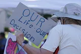 A woman holding a sign that says “Our life our decision.”
