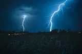 Two giant bolts of lightning strike down from the night’s sky over a nearby residence