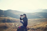 a woman with binoculars, sitting near a mountain hiking trail