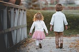 A young boy walks with his younger sister beside him