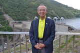 Jeffrey Fong poses in front of a railing overlooking a large concrete dam.