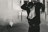 A man on a smoke-filled street ties a cloth around his face to protect himself from tear gas.
