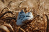 A pair of white baby shoes in dried yellow grass.