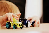 Toddler plays with toy cars on a table with face not showing. Mother struggles with boundaries with her toddler. Humor ensues.