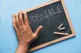 the word “impossible” on a chalkboard, and a hand hiding the “im” to make it look like it says “possible”.