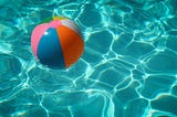 A turquoise swimming pool with a red, blue and gray beach ball in it