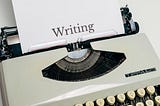 A white typewriter with a paper which says ‘Writing’ on it.