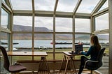 Woman working at a computer with a view of a sea inlet
