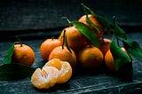 Tangerines with leaves still on, with two peeled tangerines opened in half in the foreground.