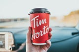 A Tim Hortons paper coffee cup held in the hand inside a car.