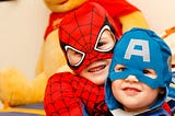 Two toddlers wear Spiderman and Captain America superhero outfits