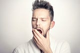 A man in a white background yawning because he has to work.