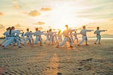 Group of students in white doing taekwondo on the beach