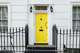 Photo of a closed yellow door/white building.