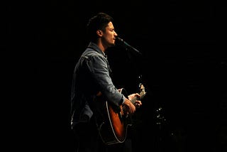 A man playing an acoustic guitar while singing into a microphone.