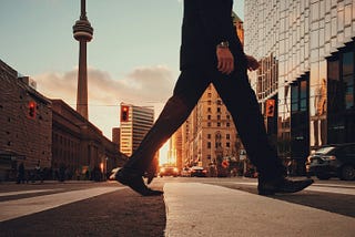 Close-up, waist on down, of man walking across the street in a big city.