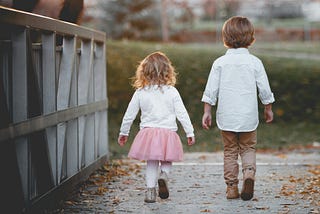 A young boy walks with his younger sister beside him