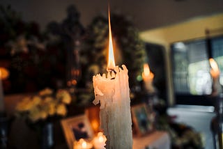 A candle burning with pictures used as an altar in the background