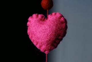Magenta heart stitched and felted, hanging on a thread.