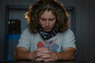 a young man with long hair folds his hands in prayer