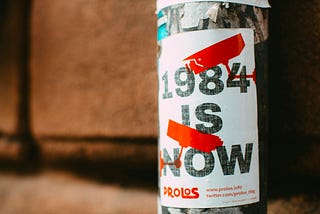 a poster taped on a pole that reads “1984 is now”