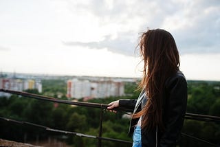 Young woman in black leather jacket standing on balcony of her building