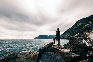 man standing on rock and overlooking water