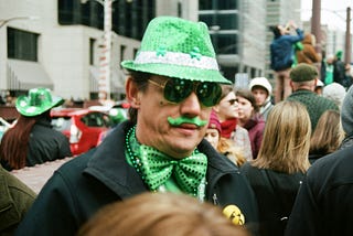 A coloured image showing a man wearing dark glasses, a green hat and a green bow tie. He also has a green moustache.