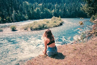 A girl sits on the river bank far from anywhere