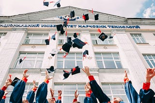 Several graduates throwing their mortarboards in the air in front of a white building