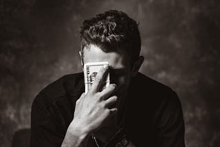Man holding money in front of his head looking embarassed