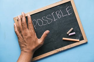 the word “impossible” on a chalkboard, and a hand hiding the “im” to make it look like it says “possible”.