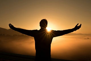 man with arms spread open, rejoicing as he watches the sunrise