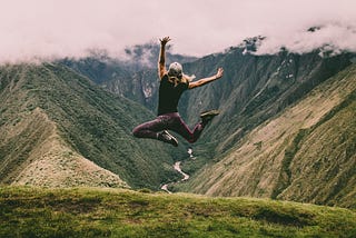 Photo of a person jumping in the air, appearing joyous against a background of rolling hills.