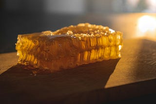 A square of honeycomb on a wooden plank, lit up with bright golden sunlight.