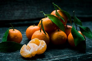 Tangerines with leaves still on, with two peeled tangerines opened in half in the foreground.