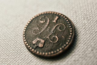 an antique coin with an unrecognizable ancient symbol on it. It is placed on a cloth backdrop.
