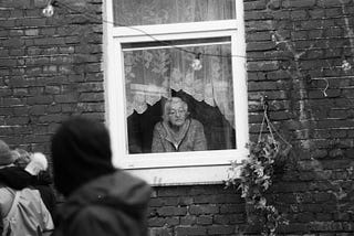 Black and white picture of old lady looking out of her window