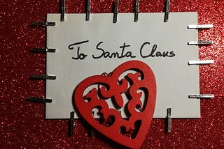 A letter addressed to Santa Clause, stapled to a glittery, red background with a red, cut-out paper heart. Photo by Zara Photo on Unsplash.