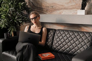 woman working on a laptop sitting on a black couch