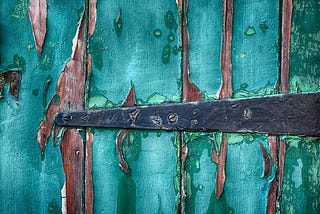 door hinge on a wooden door with teal peeling paint