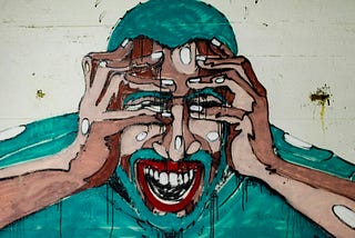 A close up of a graffiti detail depicting a person screaming or laughing as both hands cover the upper half of their face with fingers spread apart.