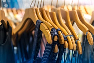 Identical blue tops hanging on a row of wooden hangers.