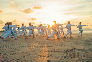 Group of students in white doing taekwondo on the beach