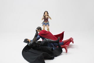Batman and Superman fighting on the floor, while Wonder Woman looks on in the background.