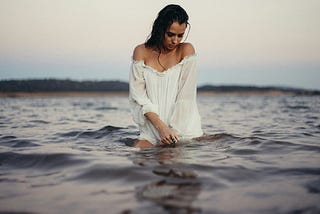 Woman dressed in white, in the ocean, water up her thighs.