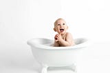 A baby boy sitting in a white clawfoot tub.