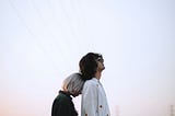 man looking at sunset with a floral shirt on and weird glasses with woman leaning her head into his back.