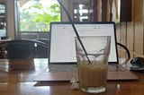Macbook Air, mouse and a glass of iced coffee on a wooden table in a cafe in Asia.