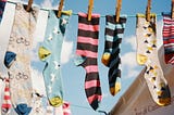 Colourful, patterned socks pegged onto a washing line against a backdrop of blue sky and clouds.